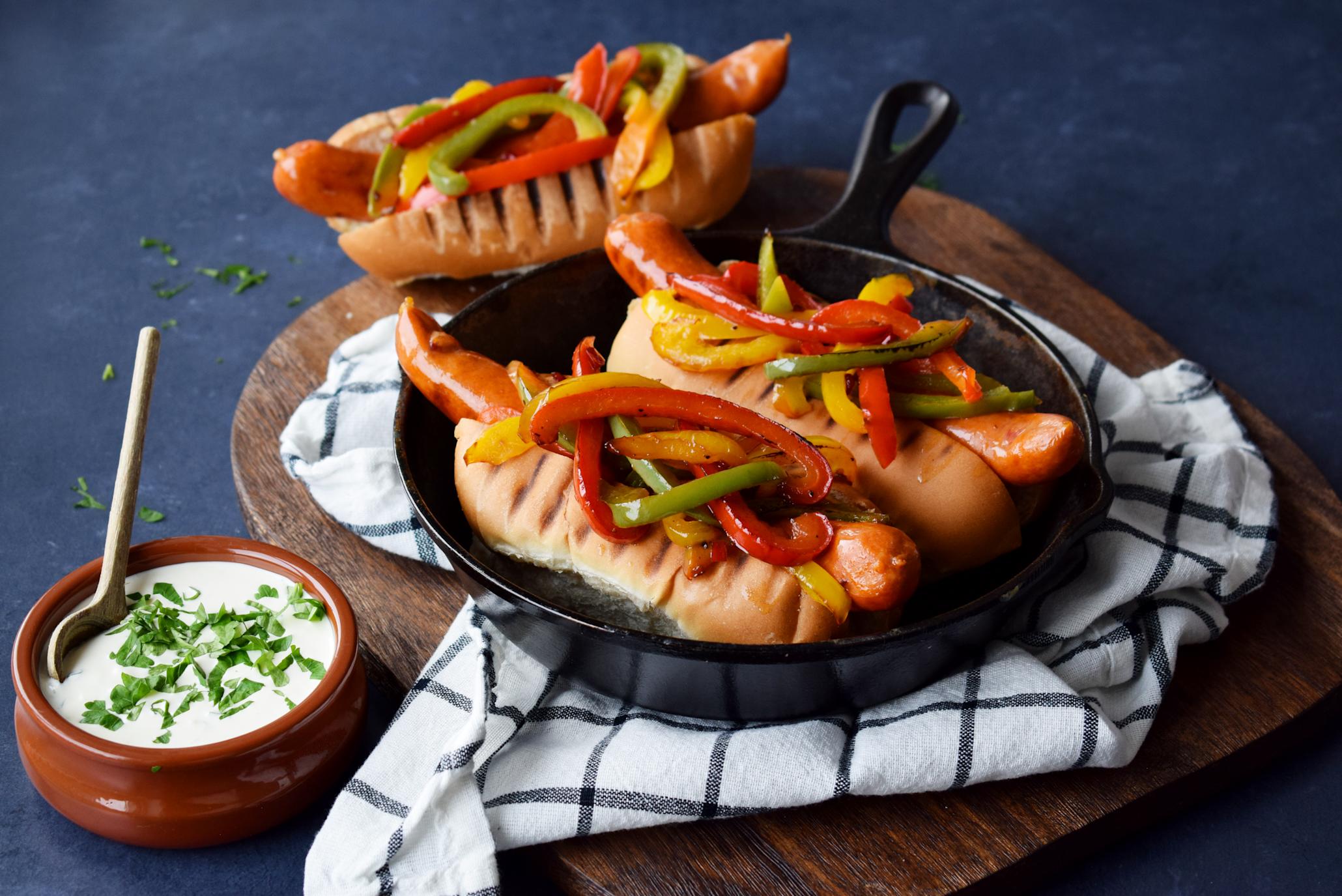 Grillet Spicy chicken pølse i pølsebrød, med honning-grillet paprika i rødt, grønt og gult med chili, servert i støpejernspanne. Hjemmelaget hvitløksdressing i liten skål på siden.