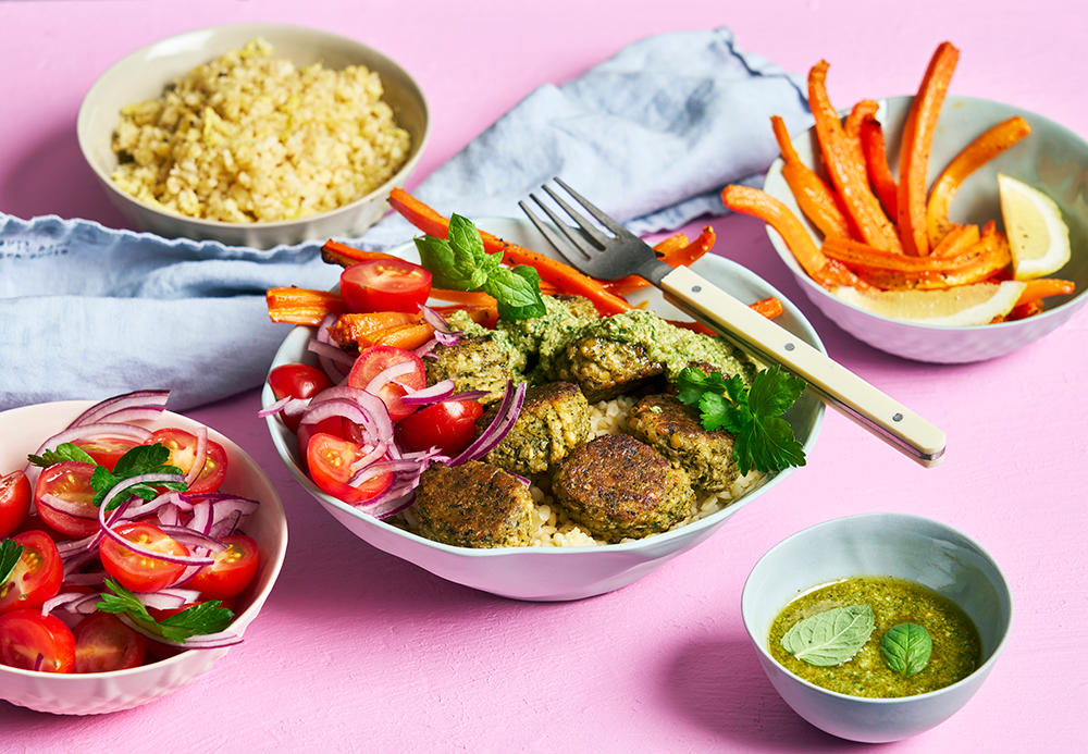 Falafel bowl med sitronstekte gulrøtter og myntepesto, servert i bolle med bulgur og tomatsalat. Små boller med tilbehør ved siden av.