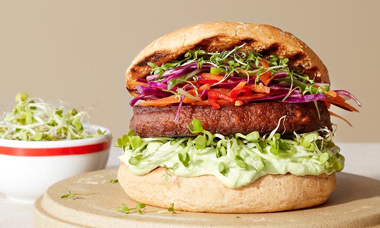 Juicy vegetarburger med rødkålslaw, avokadomos og ferske urter. Liten skål med spirer i bakgrunnen.