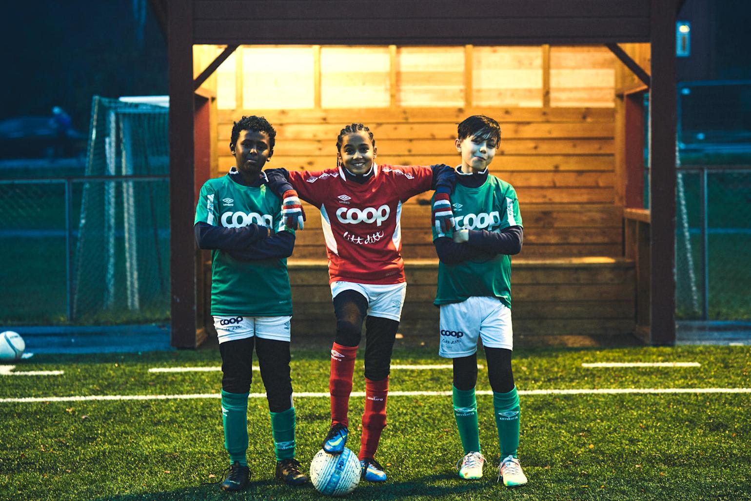 tre barn står på en fotballbane og smiler