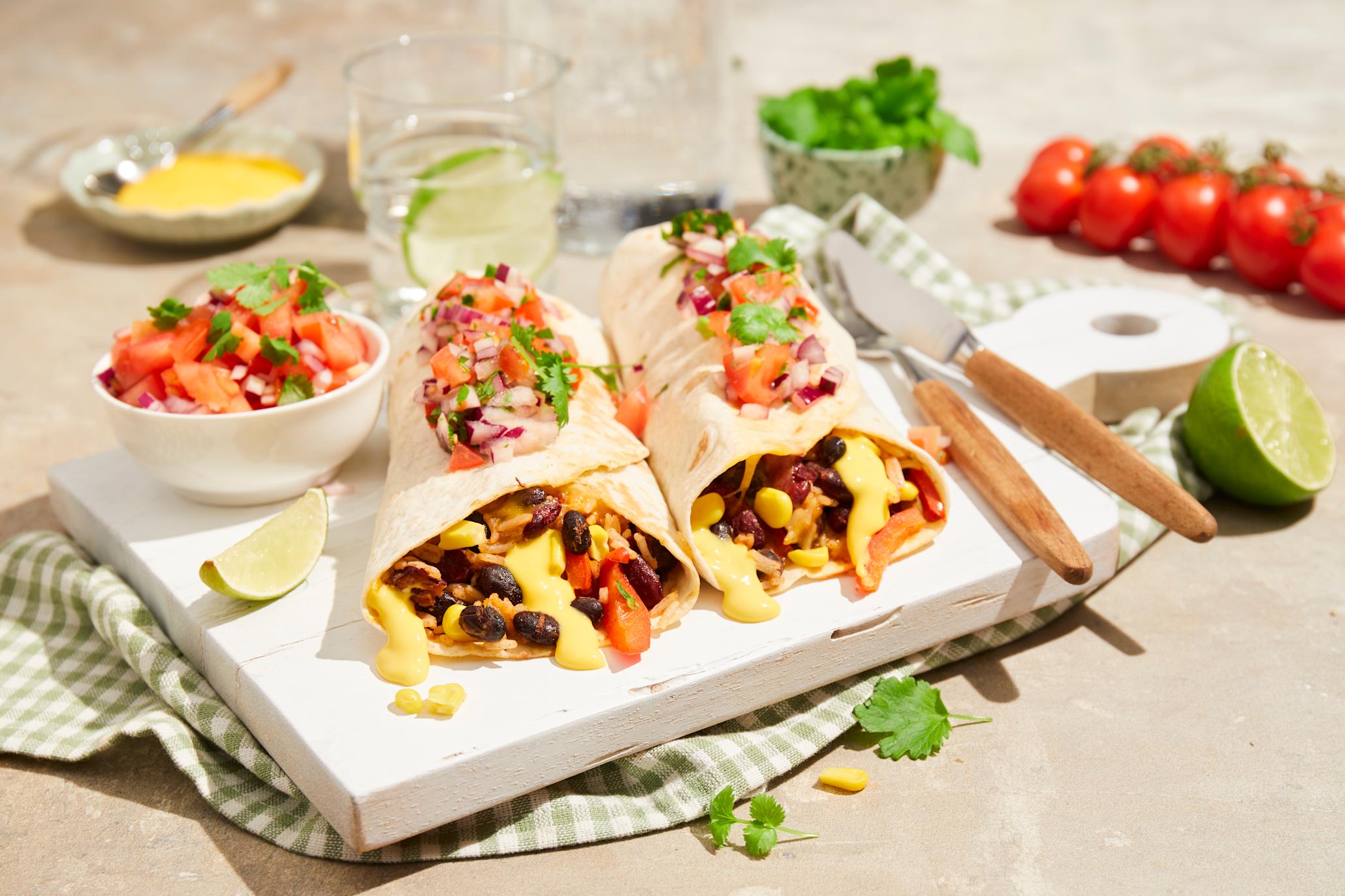 Vegetar burrito med krydrede bønner og Kavli Cheddar Dipp servert på hvit trefjøl med hjemmelaget tomatsalsa på toppen. Liten hvit skål med tomatsalsa ved siden av, og skål med cheddar dipp i bakgrunnen.
