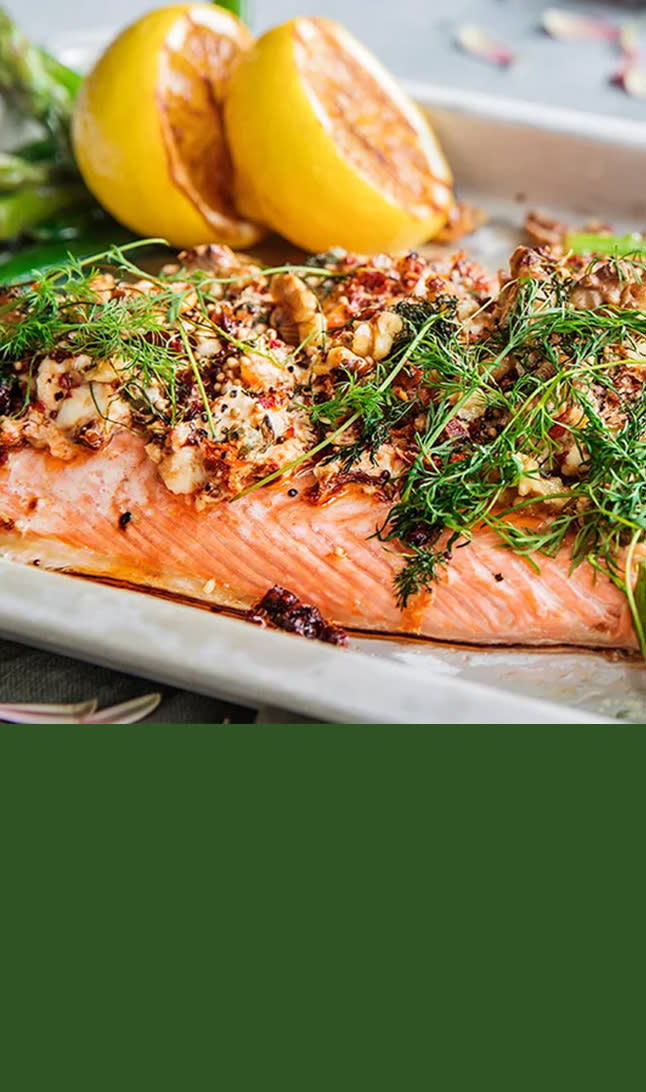 Laksefilet pyntet med urter ved siden av to havle sitroner.  grønn bakgrunn på bunnen av bilde