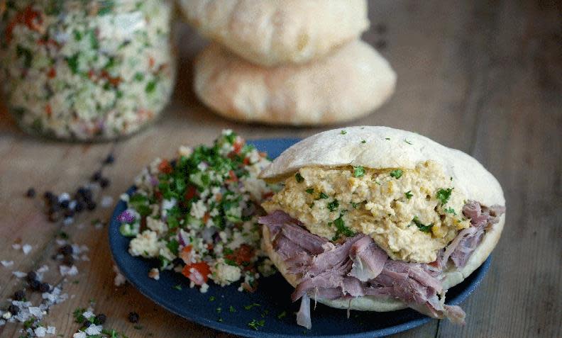Restekebab av lam med hummus og tabbouleh, på mørk blå tallerken på trebord. Pitabrød og et glass med fargerik i tabbouleh i bakgrunnen.