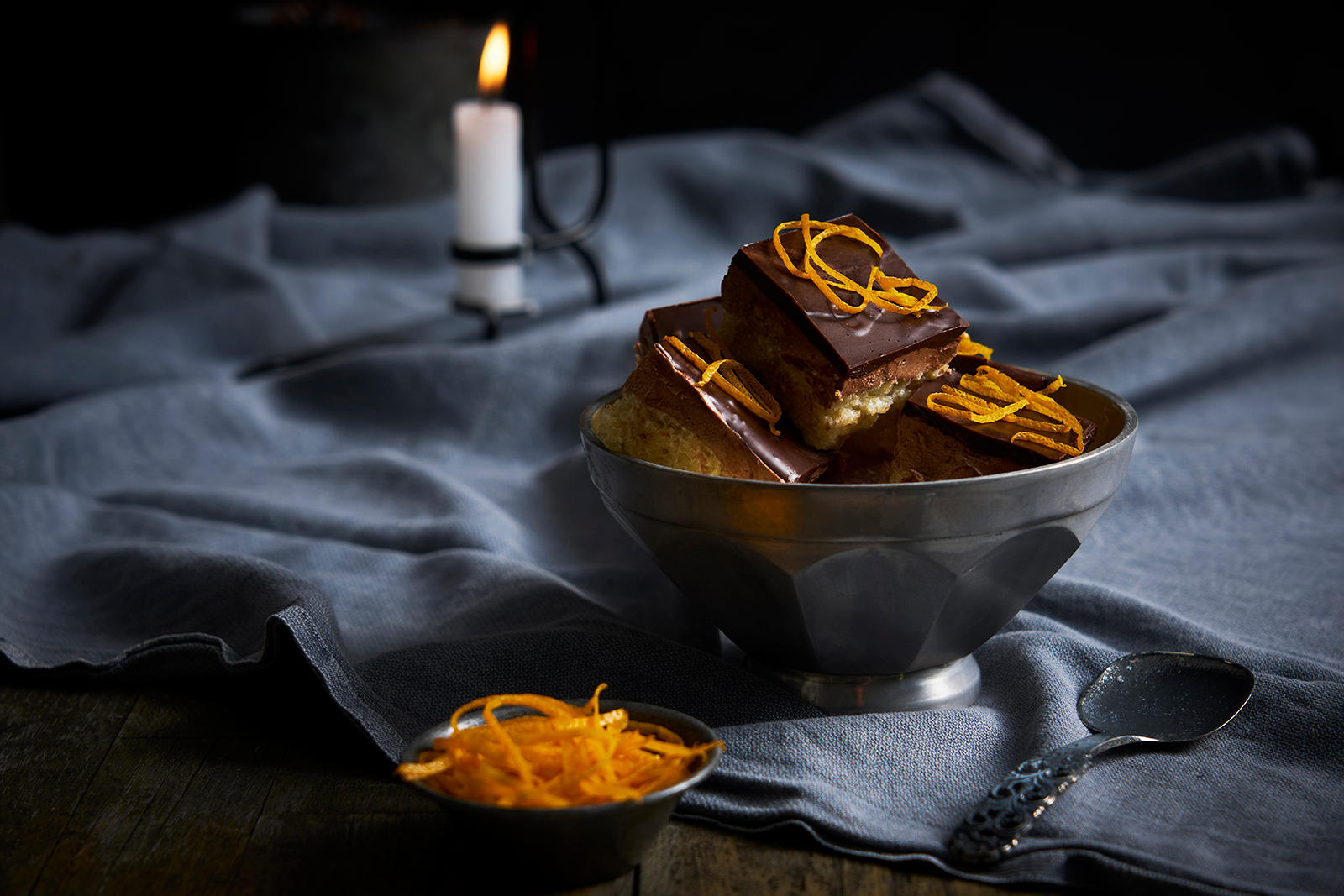 Sarah Bernard med appelsin delt i ruter og servert i metallskål på bord med mørk duk. Liten skål revet appelsinskall ved siden av.