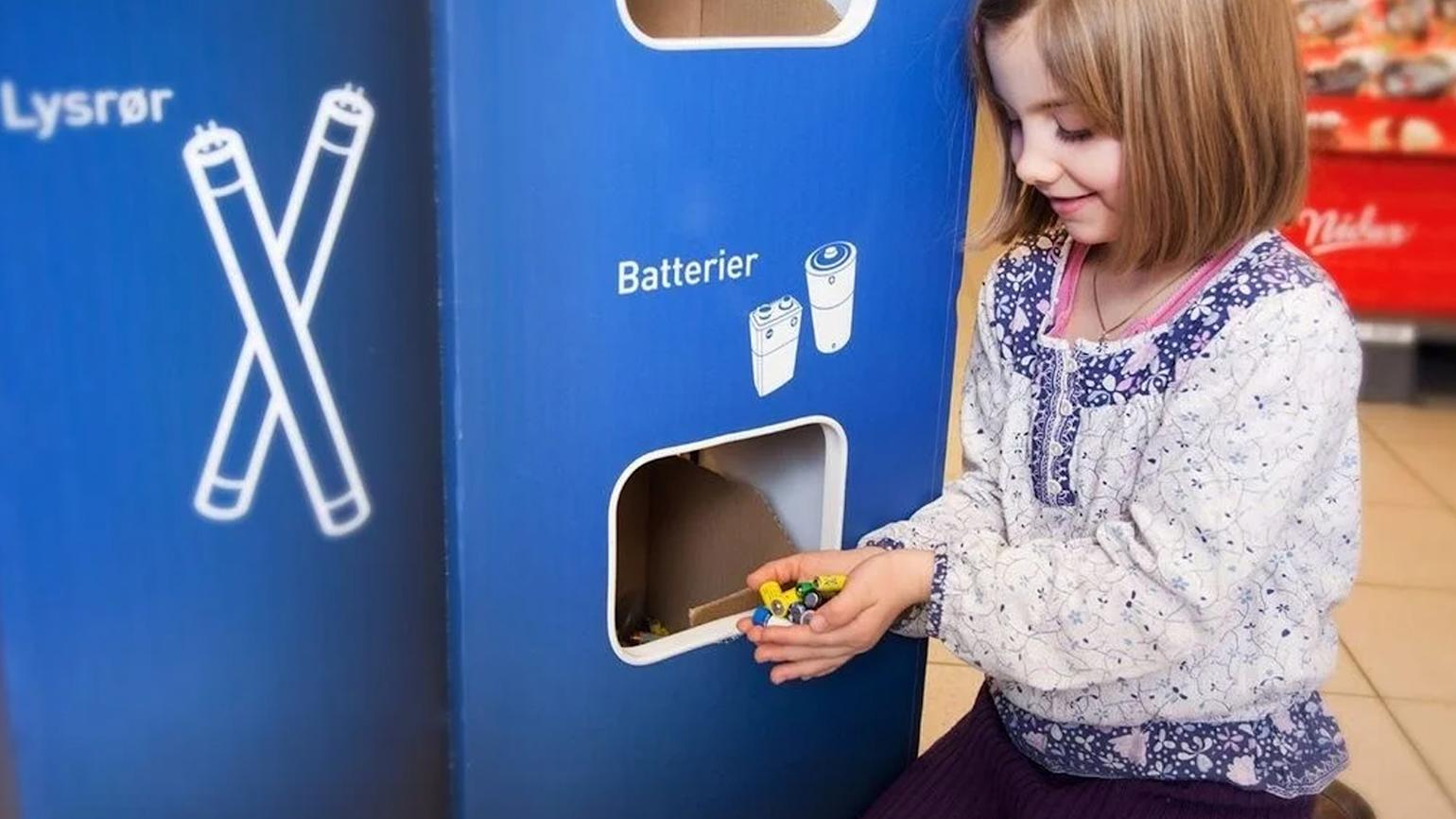 Jente sitter på knærne i butikk og putter batterier i returpunkt